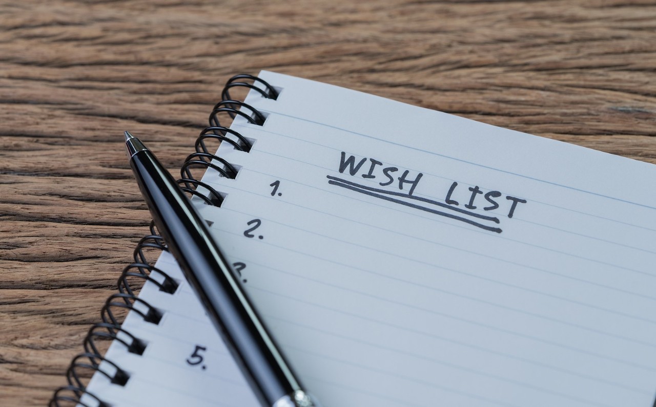 Wish list concept, pen on white paper note pad with handwritten headline as Wish List and numbers listed on wood table in soft tone, things wanted or next time purchase.
